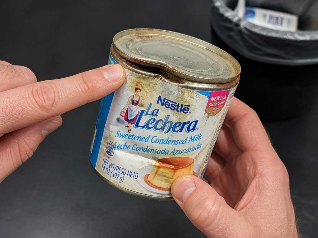 Bulging, dented, and rusted can of sweetened condensed milk ready for disposal.